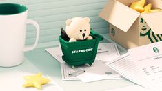 there is a starbucks bear sitting in a green cup on the table next to some papers