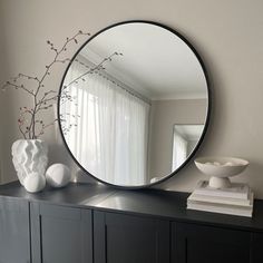 a mirror sitting on top of a black dresser next to a vase with flowers in it