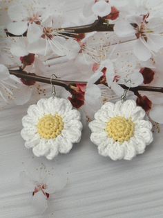 two crocheted white and yellow flower earrings on a branch with flowers in the background