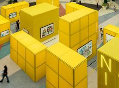 people are walking around yellow cubes in the middle of an open area with pictures on them