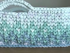 a blue and white crocheted basket sitting on top of a wooden table next to a wall