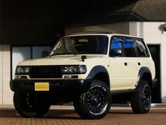 a white suv parked in front of a building with large tires on it's tires