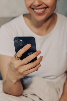 a woman smiles as she holds her cell phone in one hand and looks at the camera