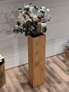 a tall wooden vase filled with flowers on top of a hard wood floor next to a wall