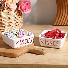 two small white bowls filled with candy sitting on top of a wooden table next to a basket