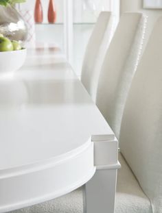 a white dining room table and chairs with fruit on the plate in front of them