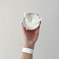 a woman's hand holding a small white bowl with an angel decoration on it