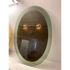 an oval mirror with three lights on the wall above it and a yellow vase behind it