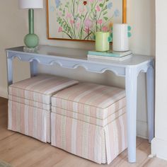 a white bench sitting in front of a painting on the wall next to a lamp