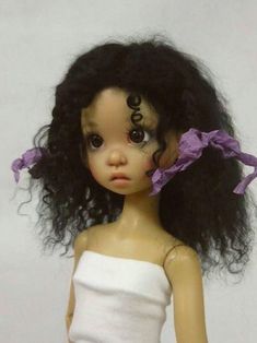 a doll with curly hair wearing a white top and purple ribbon around it's head