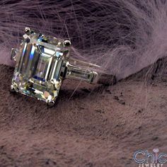 an emerald cut diamond ring on top of fur