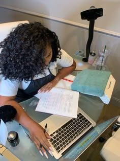 a woman sitting at a table with a laptop and notebook in front of her, writing