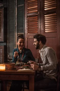 two people sitting at a table with food and drinks in front of them by an open window