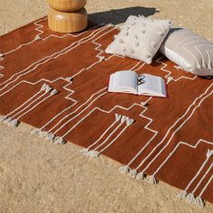 an orange and white rug on the ground with two pillows, a book and a wooden stool