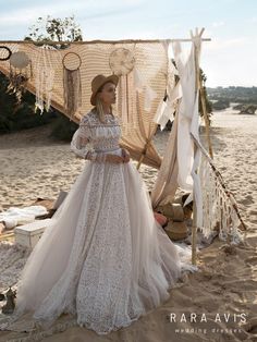 a woman in a white dress and hat standing on the beach next to a tent