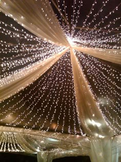 the ceiling is decorated with lights and drapes for an outdoor wedding reception at night