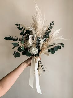 a person is holding a bouquet with flowers and leaves in their hand, against a white wall