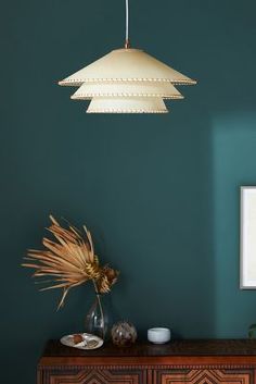 a green wall with a wooden cabinet and lamp hanging from it's sideboard