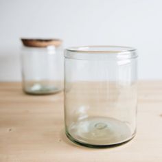 two empty glass jars sitting on top of a wooden table next to a brown lid