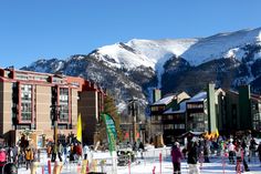 skiers and snowboarders at the bottom of a ski slope with mountains in the background