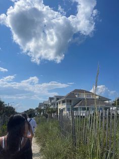 two people walking down a path next to tall grass and beach houses in the background