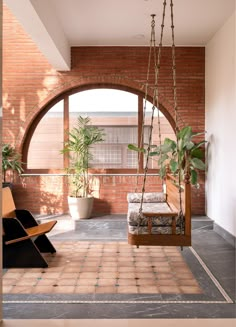 a porch with a swing chair and potted plants on the back wall, next to an arched window