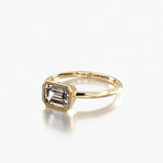 a rose gold engagement ring with an emerald cut diamond in the center, on a white background