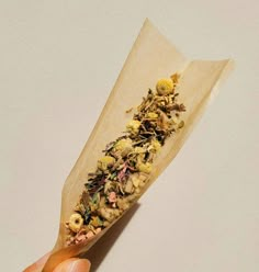 a hand holding a piece of paper with dried flowers on it and the tip of its end sticking out