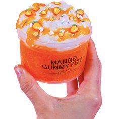 a hand holding an orange dessert in a plastic container with whipped cream and fruit toppings on top