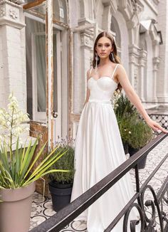 a woman in a white dress is standing on a balcony next to potted plants