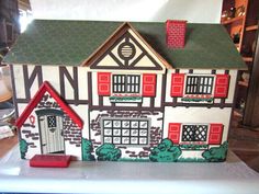 a doll house with red shutters and green roof on top of a white table