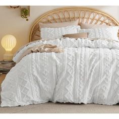 a bed with white comforter and pillows in a room next to a wicker headboard