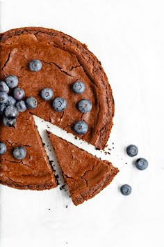 a chocolate cake topped with blueberries on top of a white table next to a slice cut from it