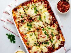 a casserole dish with meat, cheese and sauces on the table next to it