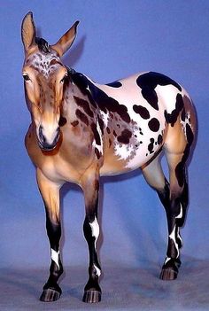 a toy horse standing on top of a white floor next to a blue wall with black spots