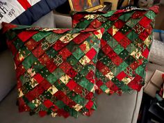 two quilted christmas blankets sitting on top of a couch next to a painting and pillows