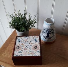 a wooden table topped with a vase next to a potted plant on top of it