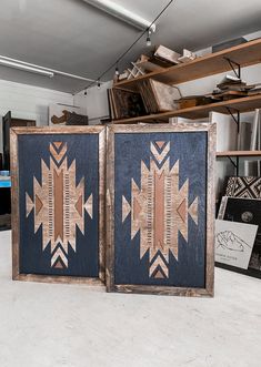 two framed art pieces sitting next to each other on top of a table in a room