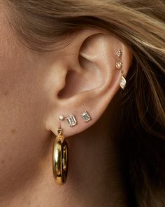 a close up of a person with ear piercings on their ears and wearing gold jewelry