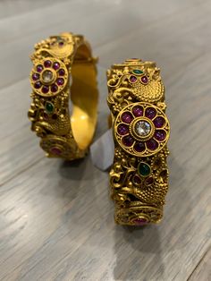 Temple bangle in matte gold and ruby stone. Detailing has the Rajasthani similarity. About an inch wide. Disclaimer: Price listed is for a single Kada. If you want to get them in a pair please select quantity 2. Festive Gold Bangle With Stone Setting, Festive Gold Bracelets With Stone Setting, Gold Bracelet With Stone Setting For Festivals, Gold Bracelets With Stone Setting For Festivals, Elegant Gold Bracelet With Peacock Design, Formal Temple Jewelry Bangle With Jewels, Formal Temple Jewelry Bangle Jeweled, Elegant Gold Bracelets With Peacock Design, Festive Gold Bangle With Peacock Design