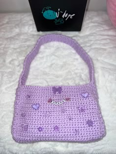 a purple crocheted purse sitting on top of a bed next to a box