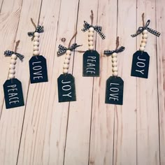 four tags with the words love, peace and joy hanging from string on wood planks