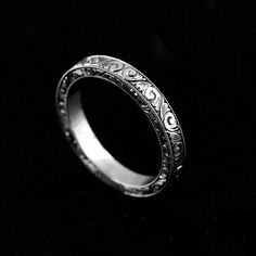 a silver ring with intricate designs on it's sides, against a black background