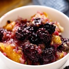 a close up of a bowl of food with berries on it and blueberries in the background