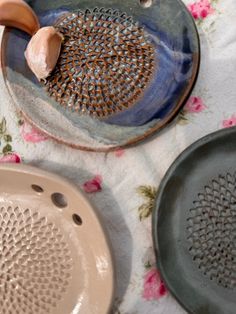 three ceramic dishes on a flowered tablecloth with an onion and garlic in the center