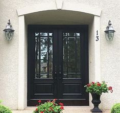 two black double doors and some flowers in front of the entrance to a house with white walls