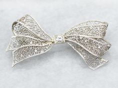 Add a touch of elegance and whimsy to any outfit with this bow brooch. The delicate filigree detailing and sparkling European Cut diamond make this brooch a timeless statement piece. Perfect for any occasion!Metal: 14K White GoldGem: European Cut Diamond .10 Carats, SI1 in Clarity, I in ColorGem Measurements: 3.2 mm, RoundMeasurements: 44 x 23 mmMarks: "X14K" Stamped on the pin guard Diamond Filigree Brooches As Gift, Elegant Wedding Jewelry With Decorative Bow, Elegant Brooches For Vintage Events, Silver Bow Brooch For Wedding, Elegant Filigree Brooches For Evening, Elegant Diamond Accented Brooch Gift, Elegant Diamond Accents Brooch For Gift, Elegant Brooch With Diamond Accents As Gift, Elegant Diamond Accented Brooches For Gifts