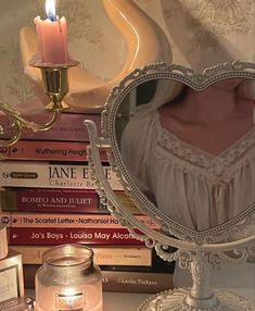 a heart shaped mirror sitting on top of a table next to a candle and books