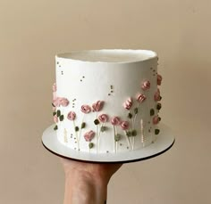 a hand holding a white cake with pink flowers on it