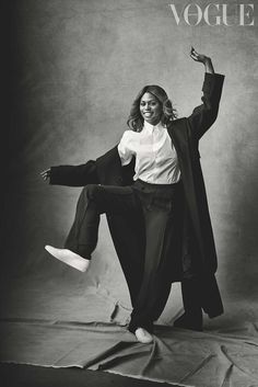 a black and white photo of a woman in a long coat dancing with her legs spread out